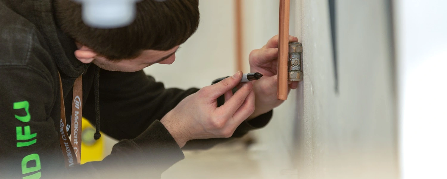 A Plumbing student measure a pipe in the workshop