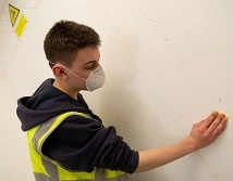 A student sanding a wall